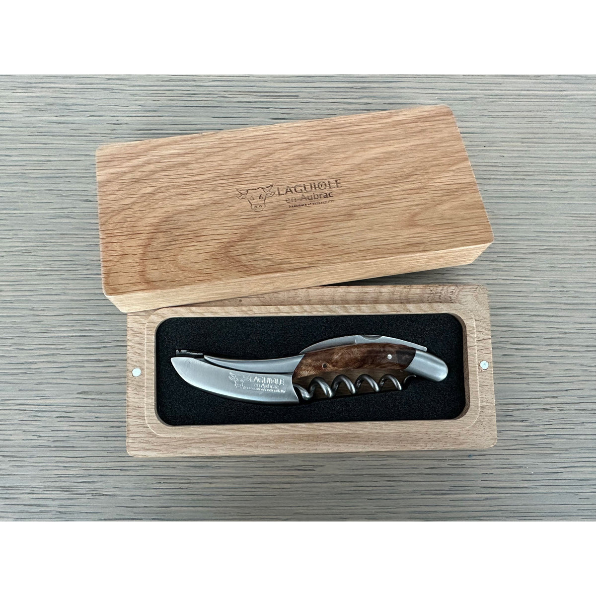 Corkscrew inside its open oak box on a grey surface