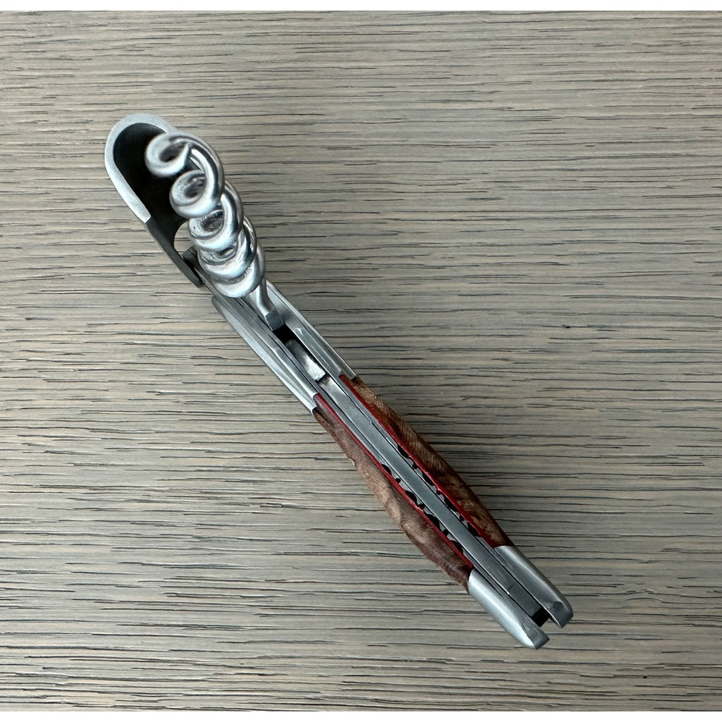 Folded corkscrew on a grey surface with the foil cutter end visible