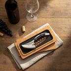 Boxed corkscrew on linen beside a wine bottle, glass and grapes