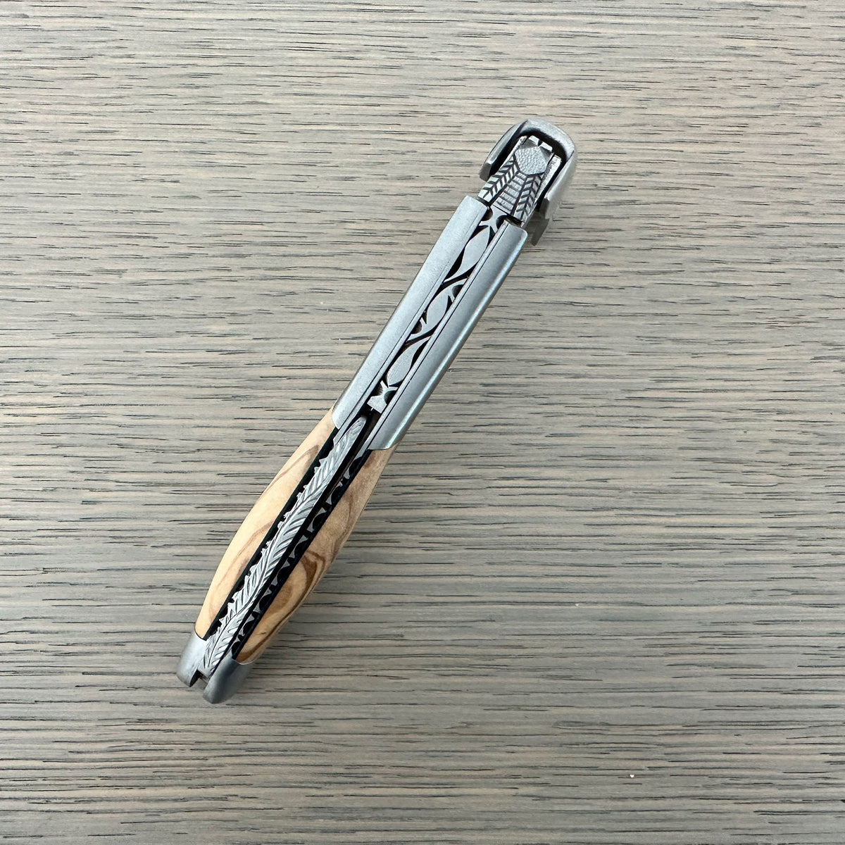 Folded olive wood corkscrew lying diagonally on a grey surface