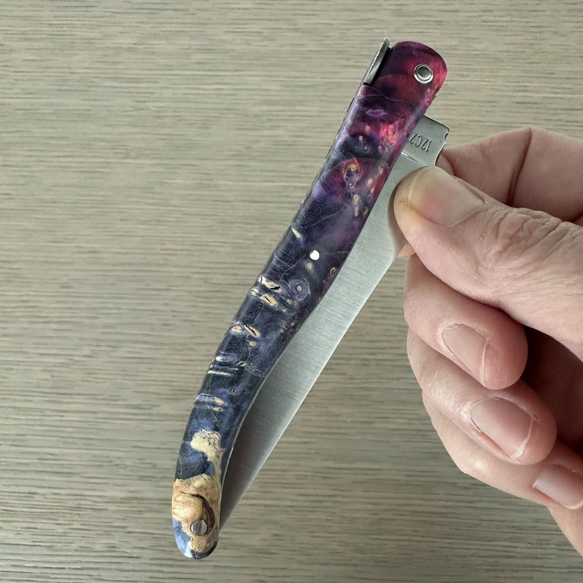 Hand folding the knife to show the purple burl handle