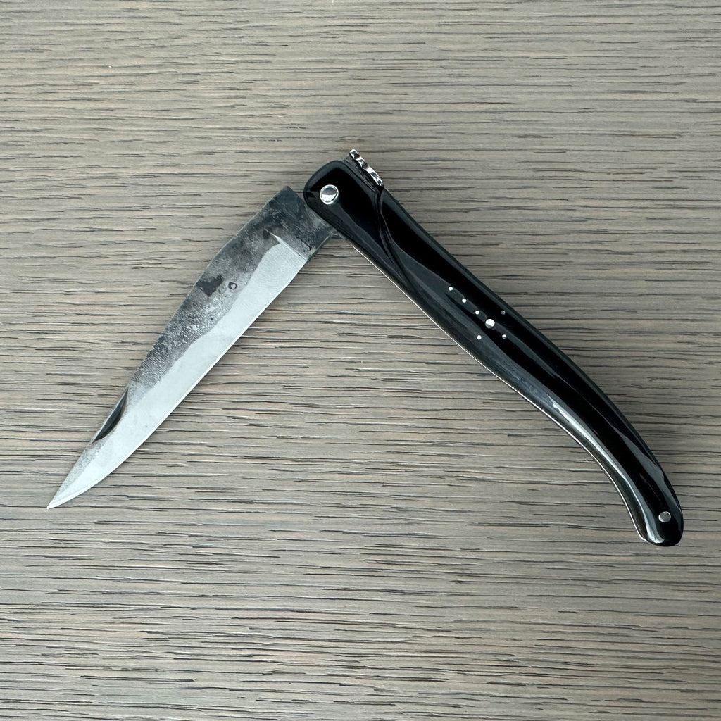 Laguiole rough forged folding knife with black buffalo horn handle on pale wood
