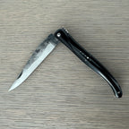 Laguiole rough forged folding knife with black buffalo horn handle on pale wood
