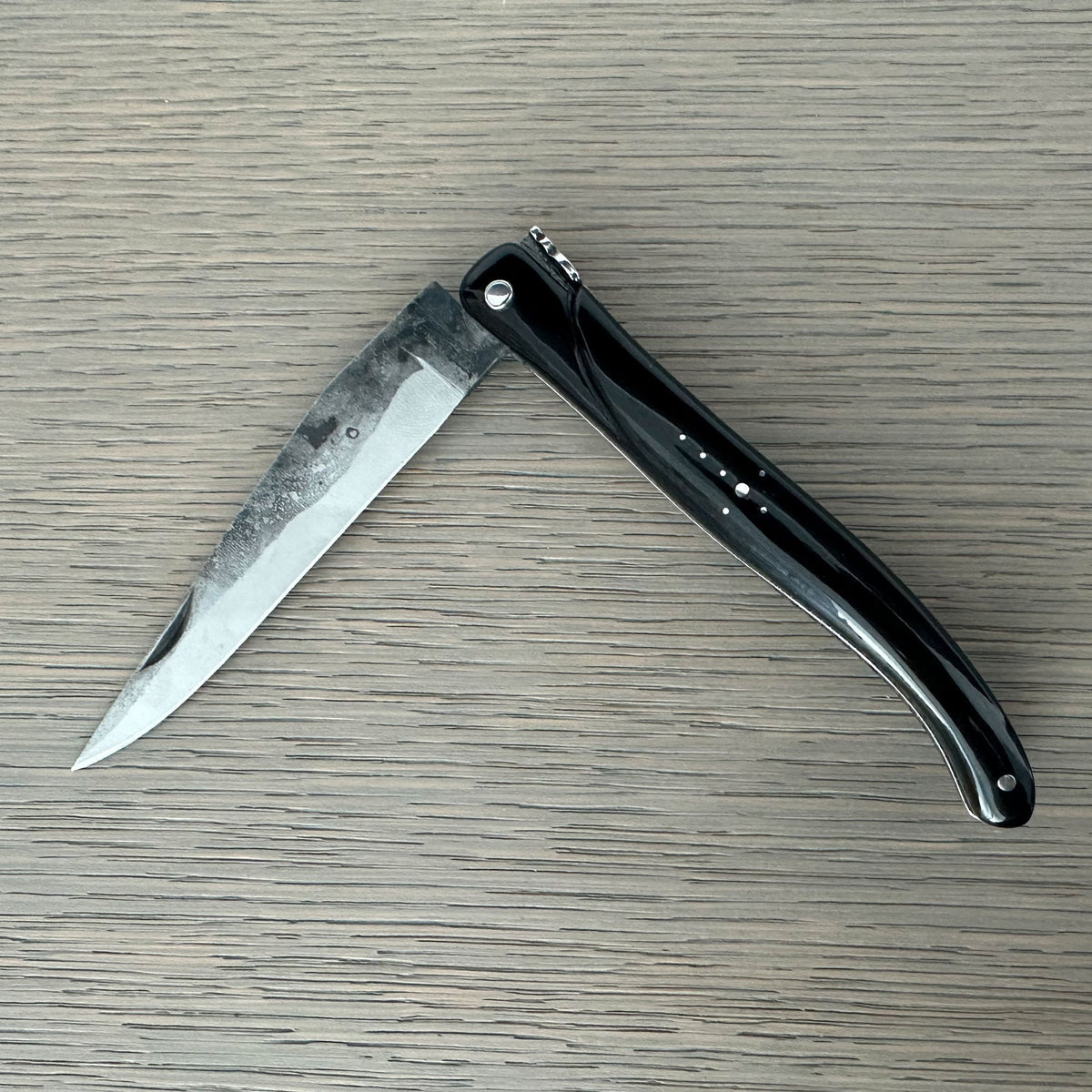 Laguiole rough forged folding knife with black buffalo horn handle on pale wood