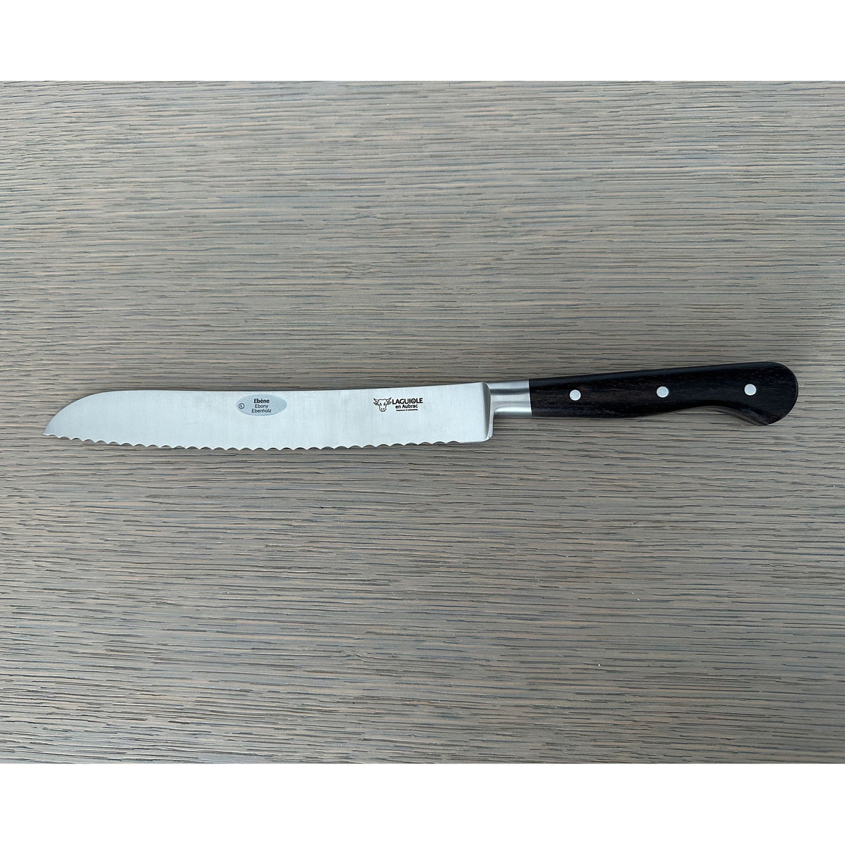Laguiole forged bread knife with black ebony handle on a grey wood surface