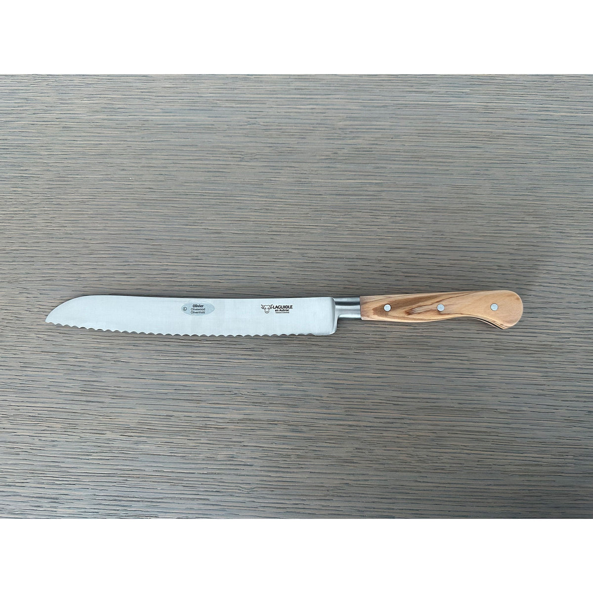 Laguiole forged bread knife with olive wood handle on a grey wood surface