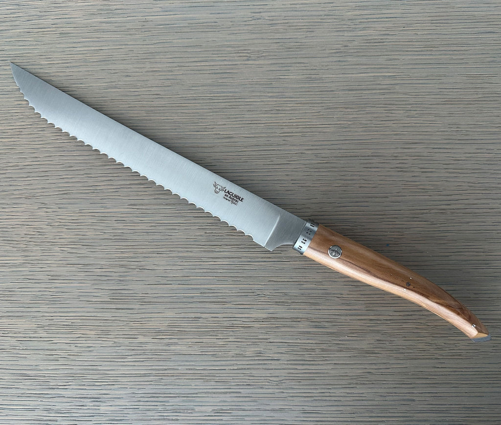 Laguiole serrated bread knife with olive wood handle on a grey wood surface