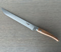 Laguiole serrated bread knife with olive wood handle on a grey wood surface