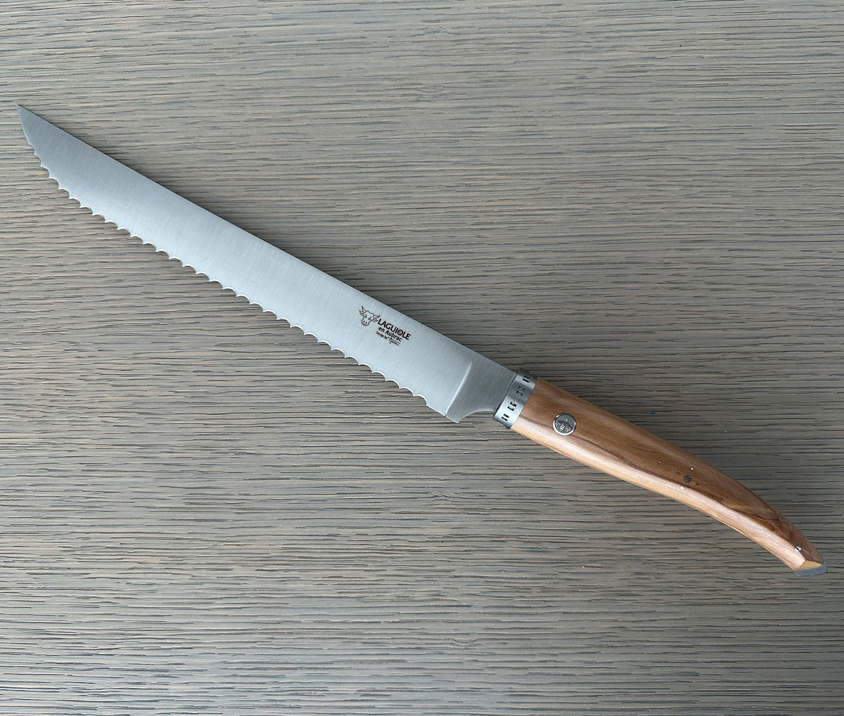 Laguiole serrated bread knife with olive wood handle on a grey wood surface