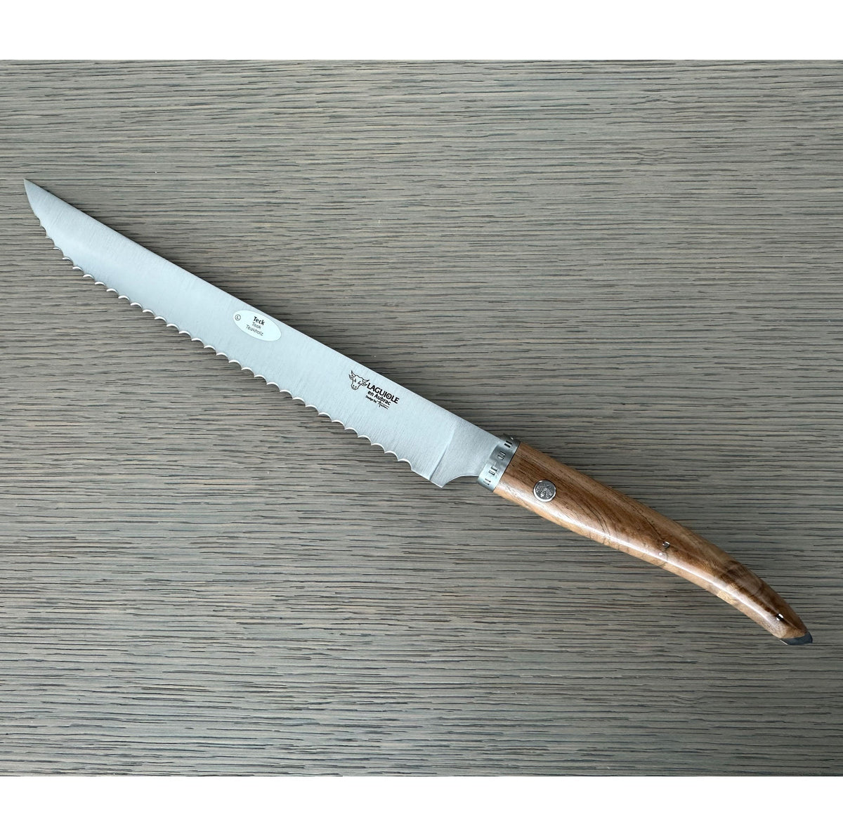 Laguiole serrated bread knife with teak handle on a grey wood surface