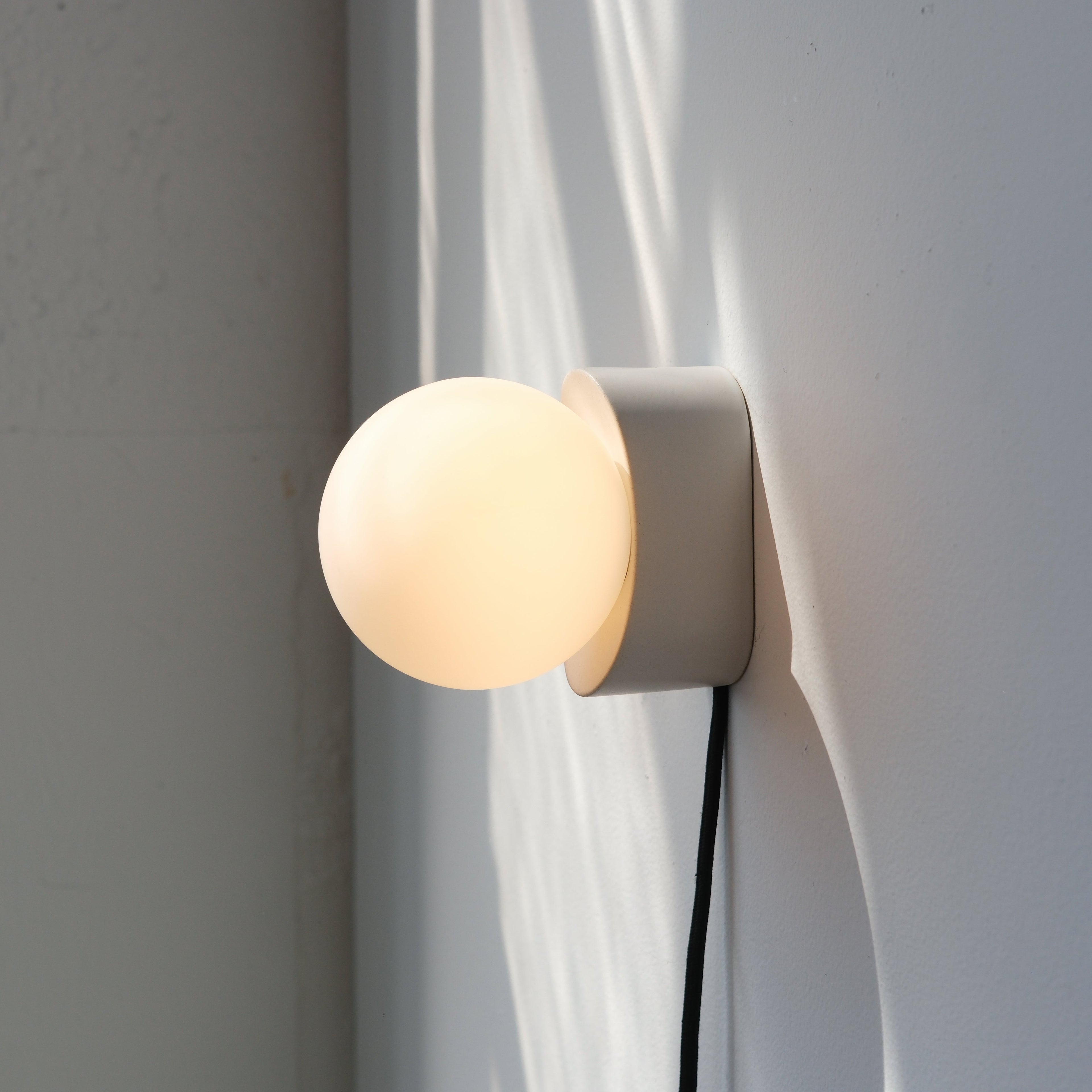 Iota Sconce in black matte glaze beside a bed